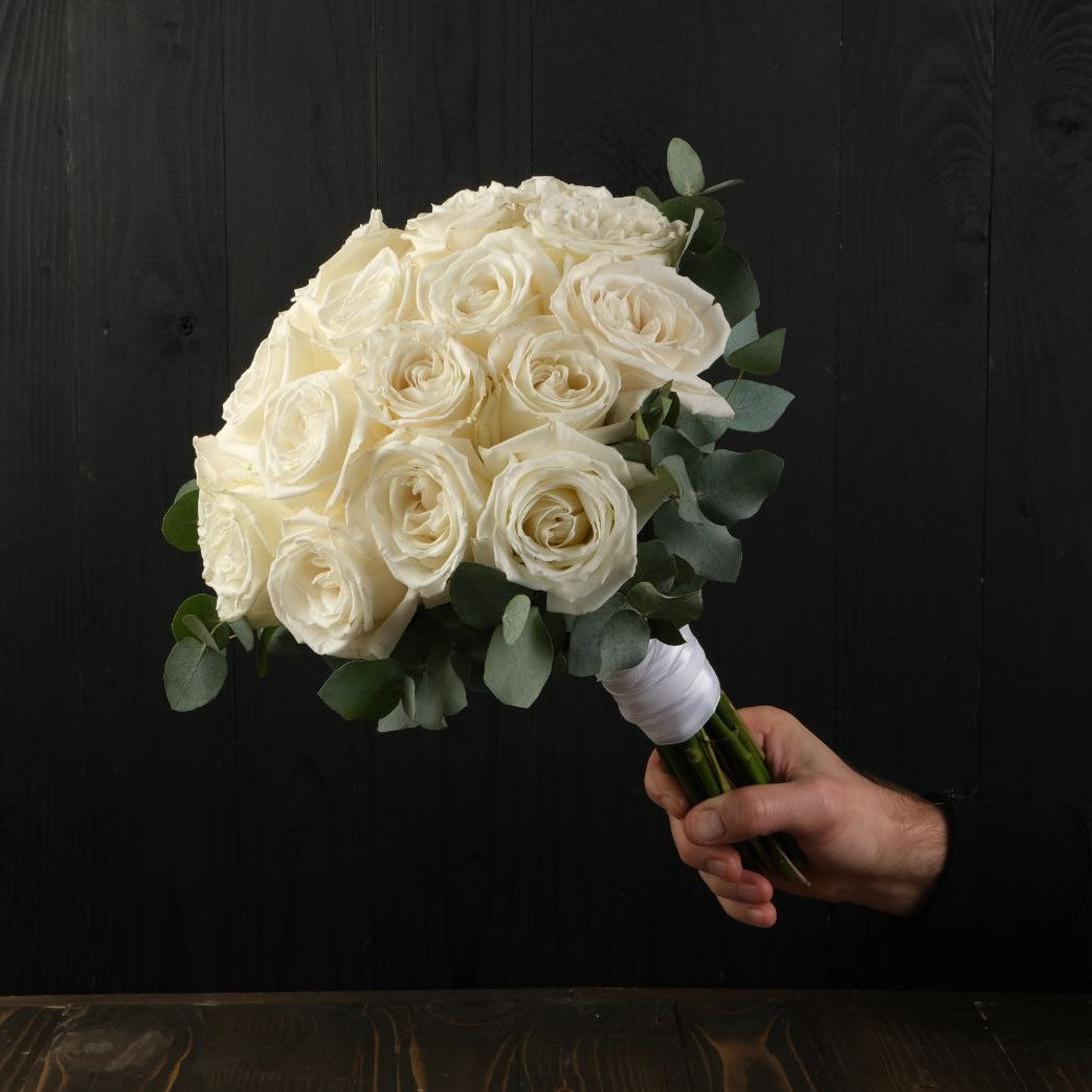 Bouquet of white roses held by a hand against a black background